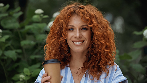 cheerful redhead woman holding paper cup outdoors