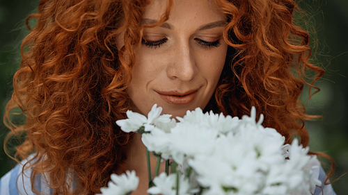 close up of curly redhead woman looking at white flowers