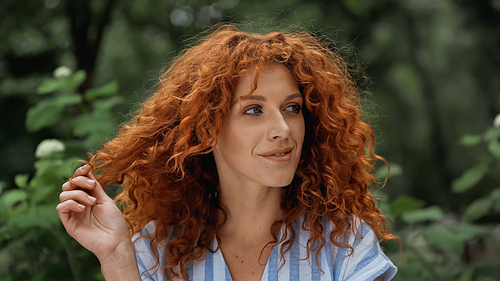 cheerful redhead woman pulling red curly hair