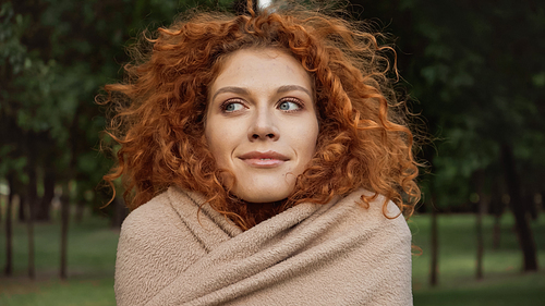 pleased redhead woman with blue eyes covered in blanket outside