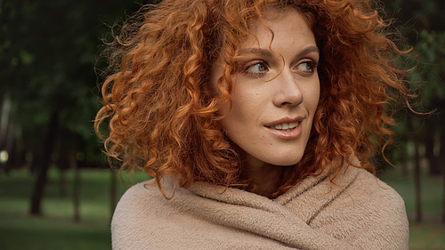 pretty redhead woman covered in blanket smiling while looking away outside