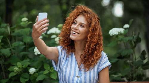 happy redhead woman taking selfie in green park