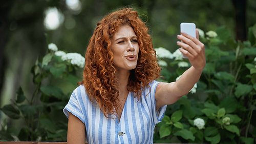 curly redhead woman taking selfie in green park