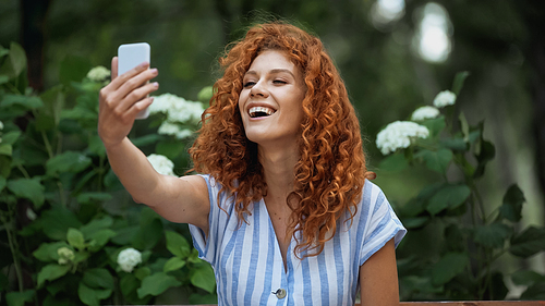 glad redhead woman taking selfie in green park