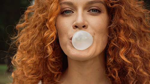 close up view of curly woman blowing bubble gum
