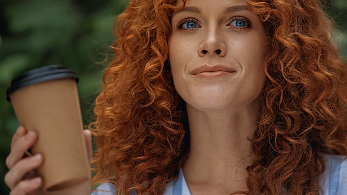 positive redhead woman with blue eyes holding paper cup outside