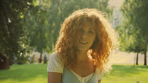 sunshine on curly red hair of woman smiling while  in park