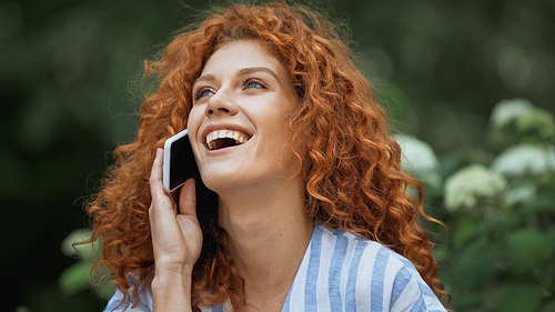 happy young woman with red hair laughing while talking on smartphone