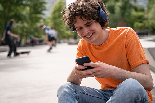 happy young man in headphones chatting on mobile phone in skate park