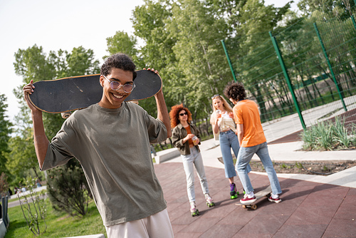 happy african american man with skateboard  near multiethnic friends