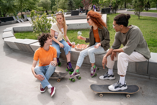 cheerful multiethnic skaters talking near tasty pizza in skate park
