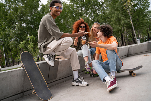 smiling african american man sitting on border near skate and happy friends