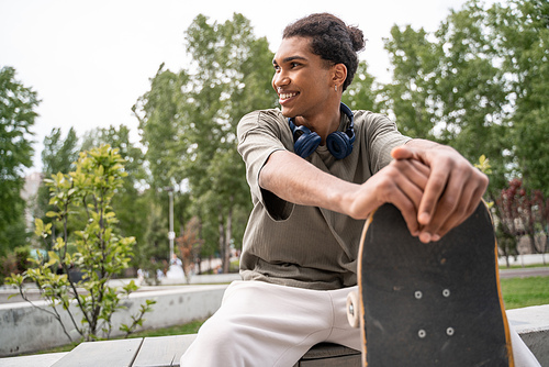 young and joyful african american skater looking away while sitting in skate park