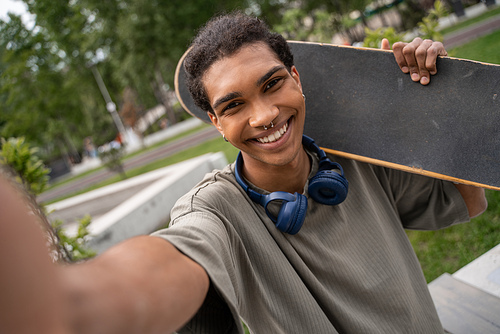 pierced african american man with headphones and skateboard smiling at camera