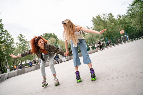 happy friends holding hands while rollerblading in skate park