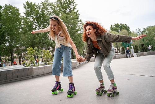 excited women holding hands while rollerblading in park