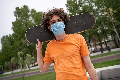 young man in safety mask looking away while holding skate behind neck