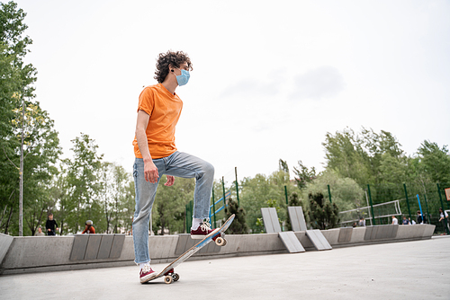 young man in medical mask riding skateboard in skate park