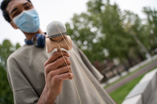 blurred african american man in medical mask playing kendama game outdoors
