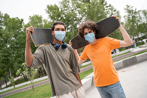 multiethnic friends in safety masks  while holding skates