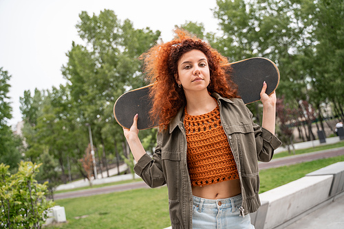 young curly woman  while holding skateboard in city park