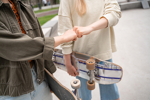 partial view of women with skateboards doing fist bump outdoors