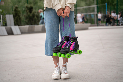 partial view of woman in jeans and sneakers holding roller skates