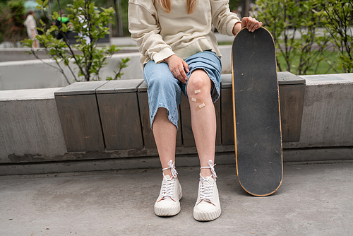 cropped view of skater with adhesive plasters on injured knee sitting on border bench