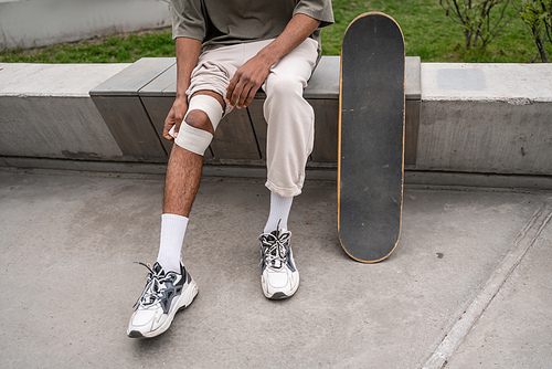 cropped view of african american man bandaging injured knee near skateboard