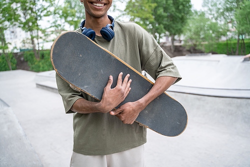 partial view of african american man smiling while holding skateboard