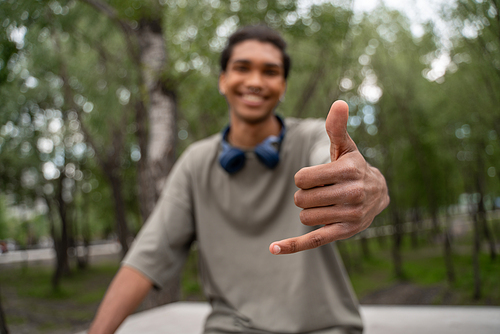 blurred african american man smiling and showing hang loose gesture outdoors