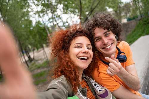 curly, happy man and woman taking selfie in park