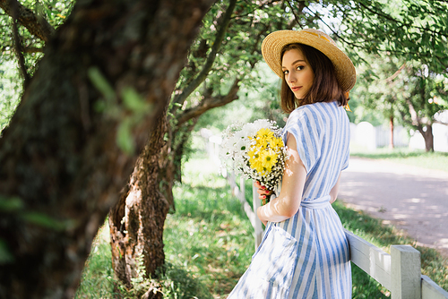 Woman in dress and straw hat holding flowers in park
