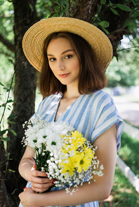 Young woman in sun hat holding flowers in park