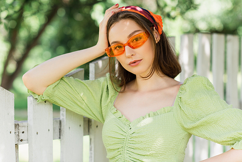 Pretty woman in headscarf and sunglasses standing near fence