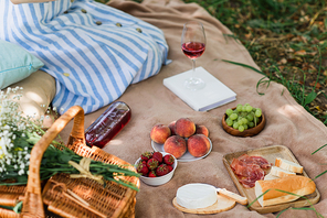 Cropped view of tasty food and wine near basket and woman on blanket in park
