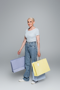 happy senior woman in jeans holding shopping bags on grey