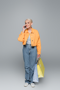 elderly woman with shopping bags smiling while talking on mobile phone on grey