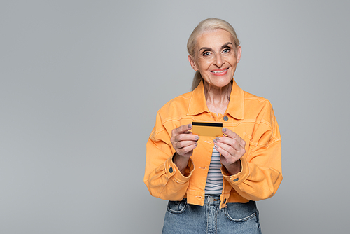 joyful senior woman holding credit card while  isolated on grey