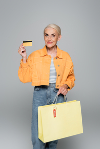 smiling senior woman with shopping bag and credit card  on grey