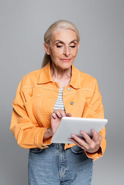 senior woman in orange jacket using digital tablet isolated on grey