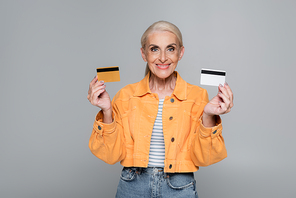 please woman in orange jacket showing credit cards isolated on grey