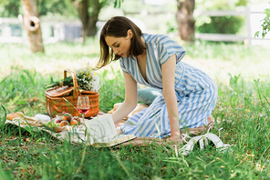 Side view of woman reading book near glass of wine during picnic in park