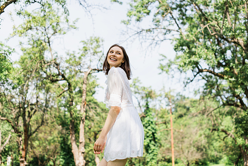 Happy woman in white dress standing in summer park