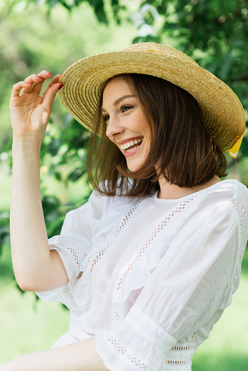 Smiling woman holding straw hat and looking away in park