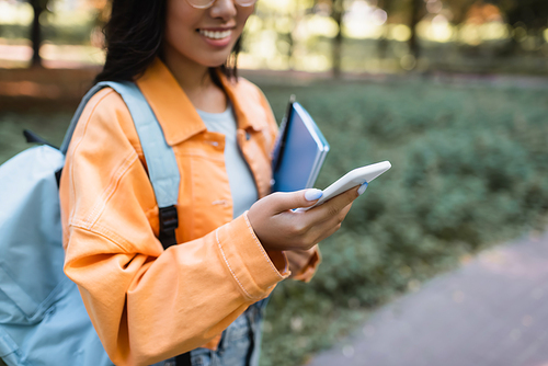 partial view of blurred woman in orange jacket using mobile phone outdoors