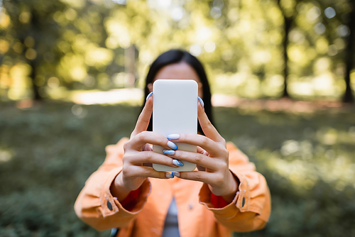 blurred woman taking selfie on mobile phone in park