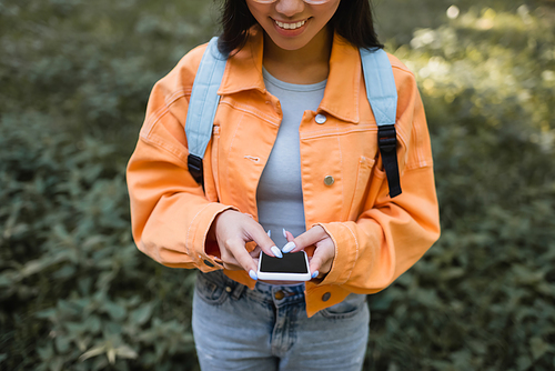 cropped view of smiling woman in orange jacket using cellphone with blank screen