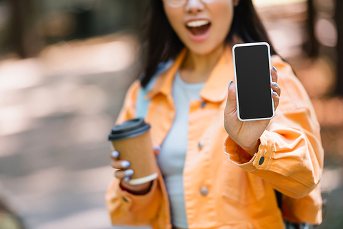 cropped view of blurred woman with paper cup showing smartphone with blank screen outdoors