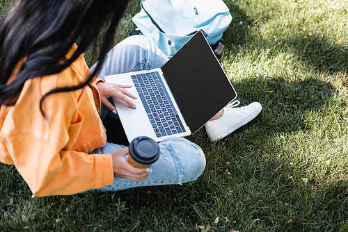 high angle view of cropped woman with coffee to go using laptop with blank screen on grass